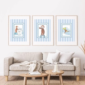 Op de afbeelding: Een set van drie ingelijste wandkunstprints met Curious George. Elke print toont een lichtblauwe achtergrond met verticale strepen en een centrale illustratie van de aap die badkameractiviteiten uitvoert, zoals handen wassen en tanden poetsen.