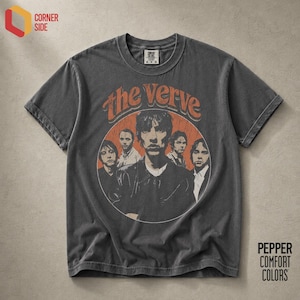 May include: A charcoal grey short-sleeved t-shirt featuring a circular graphic with a vintage-style illustration of the band The Verve. The text "the verve" is printed in an orange arched font above the circular portrait of the five band members.