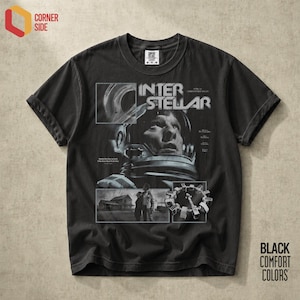Op de afbeelding: Een zwart t-shirt met korte mouwen en een grafische print van de film Interstellar. Het ontwerp bevat een grote astronautenhelm, een huis en een ruimtestation, met de tekst Interstellar en filmcredits in het wit gedrukt.