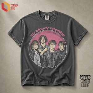 Puede incluir: Una camiseta de manga corta gris carbón con un gráfico circular sobre un fondo rosa. El gráfico muestra a cuatro personas y el texto "my bloody valentine" en letras rosas. La camiseta tiene cuello redondo y una etiqueta en el cuello.