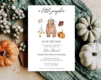 Op de afbeelding: Een baby shower uitnodiging met een aquarel illustratie van een baby outfit, een pompoen en herfstbladeren. De tekst luidt "a little pumpkin is on the way!" en bevat de datum, tijd en locatie van de babyshower.