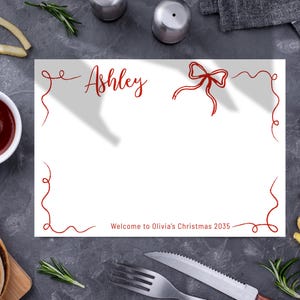 May include: A white invitation card with red decorative elements, the name "Ashley" in cursive, and a bow illustration. The text "Welcome to Olivia's Christmas 2035" is also present. The image includes food items like fries, ketchup, and a burger.