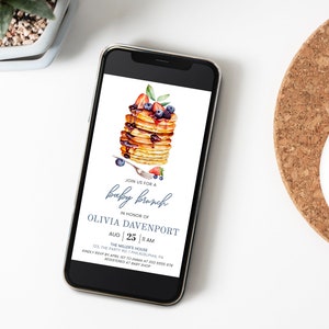 May include: A digital invitation for a baby brunch in honor of Olivia Davenport. The invitation features a watercolor illustration of a stack of pancakes with blueberries, strawberries, and maple syrup. The text reads "Join us for a baby brunch in honor of Olivia Davenport, Aug 25 | 11 AM, The Miller's House, 123 The Party Rd, Philadelphia, PA. Kindly RSVP by Aug 10 at 123-456-7890. Registered at Baby Shop."
