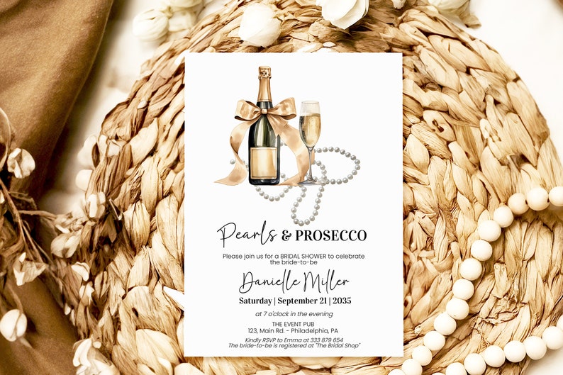 May include: A white card with a gold and white illustration of a bottle of champagne and a glass of champagne with a pearl necklace. The text on the card reads "Pearls & Prosecco" and "Please join us for a bridal shower to celebrate the bride-to-be Danielle Miller Saturday | September 21 | 2035 at 7 o'clock in the evening THE EVENT PUB 123, Main Rd Philadelphia, PA Kindly RSVP to Emma at 333 879 6654 The bride-to-be is registered at "The Bridal Shop"