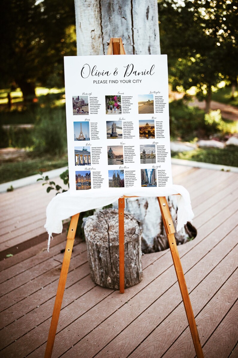 May include: A white wedding seating chart with the names Olivia & Daniel and the text "Please find your city". The chart features photos of famous landmarks from around the world, including the Eiffel Tower, Big Ben, and the Statue of Liberty.