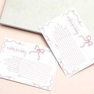 K&ouml;nnte beinhalten: Zwei wei&szlig;e Karten mit rosa Linien und einem rosa Schleifendesign. Die Karten haben den Text "wishes for baby" und Linien zum Schreiben.