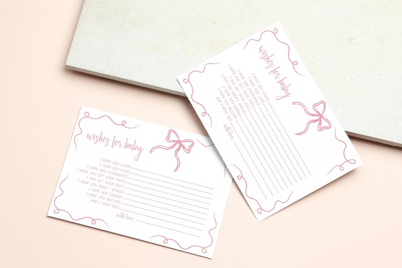 K&ouml;nnte beinhalten: Zwei wei&szlig;e Karten mit rosa Linien und einem rosa Schleifendesign. Die Karten haben den Text "wishes for baby" und Linien zum Schreiben.