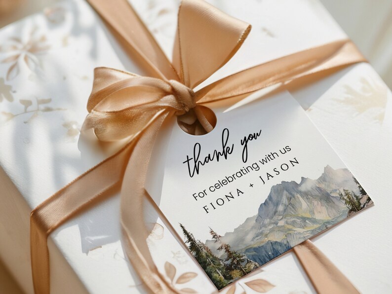 May include: A white thank you tag with a watercolor mountain scene and the text "thank you" in black cursive. The tag also includes the text "For celebrating with us FIONA + JASON".