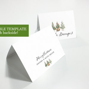 May include: A printable Christmas card template with a folded design. The front of the card features a watercolor illustration of three Christmas trees with ornaments and a burlap sack. The text "Merry Christmas Amanda & Kevin Miller" is printed on the front of the card. The back of the card features the text "The Davenport" and a watercolor illustration of three Christmas trees with ornaments and a burlap sack.