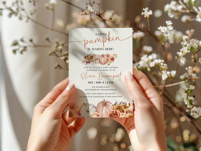 May include: A baby shower invitation with a fall theme. The invitation features a watercolor illustration of pumpkins and flowers in shades of orange, pink, and brown. The text reads "A little pumpkin is almost here!" and includes the date, time, and location of the shower. The invitation is perfect for a fall baby shower.