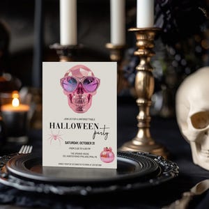 May include: A pink Halloween party invitation featuring a pink skull wearing sunglasses and a spider. The text reads "Join us for an unforgettable Halloween party, Saturday, October 31, from 2:00 to 4:00 PM, The Spookie House, 033 Haunted Road, Philadelphia, PA. Kindly RSVP by 27 October to Emma at 215-555-0000."