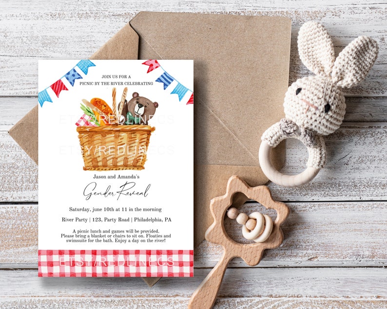May include: A baby shower invitation with a picnic theme. The invitation features a watercolor illustration of a picnic basket with a bear, food, and text. A crocheted bunny rattle and wooden rattle are also in the image.