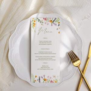 May include: A white plate with a gold fork and knife, a white linen napkin, and a floral menu card with the word "Menu" written in cursive. The menu lists a starter, entree of choice, and dessert. The menu items include organic mixed green salad with baby grape tomatoes and champagne vinaigrette, grilled beef tenderloin served with au jus, mashed potatoes and green beans, chicken pesto-crusted chicken medallions served with lemon and thyme drizzle with roasted potatoes and asparagus, and white almond cake with fresh raspberry butter cream.