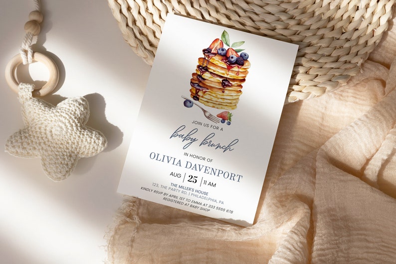 May include: A baby shower invitation with a watercolor illustration of a stack of pancakes topped with blueberries, strawberries, and maple syrup. The invitation reads "Join us for a baby brunch in honor of Olivia Davenport, Aug 25, 11 AM, The Miller's House, 123 The Party Rd, Philadelphia, PA. Kindly RSVP by April 1st to Emma at 333 555 678. Registered at Baby Shop."