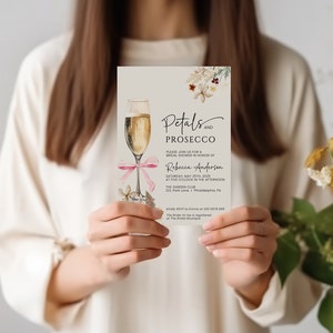 May include: A white invitation card with a watercolor illustration of a champagne flute and floral details. The text reads "Petals and Prosecco" and includes details for a bridal shower in honor of Rebecca Anderson. The event is scheduled for Saturday, May 25th, 2023 at 2:00 PM at The Garden Club, 123 Park Lane, Philadelphia, PA.