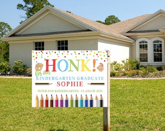 May include: A white yard sign with colorful confetti and the text "Honk! for our Kindergarten Graduate Sophie Peter Pan Kindergarten - Class of 2020". The sign also features a row of colorful pencils.