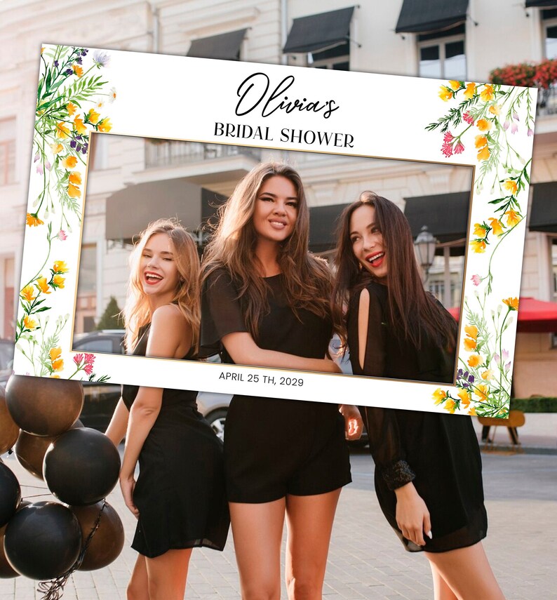 May include: A white photo booth frame with a gold border and floral accents. The frame has the text "Olivia's Bridal Shower" and "April 25th, 2029" printed on it.