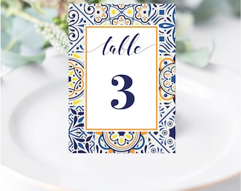 May include: Table number card with a blue and white tile pattern and orange accents. The card has the word "table" and the number "3" in a white rectangle.