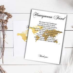 Puede incluir: Una tarjeta blanca con texto dorado y un contorno dorado de un mapa del mundo. El texto dice "Fondo de luna de miel" y explica que en lugar de regalos tradicionales, la pareja apreciar&iacute;a las contribuciones a su luna de miel. La tarjeta termina con "Gracias."
