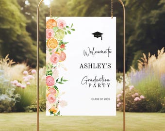Könnte beinhalten: Ein Schild für eine Abschlussfeier mit dem Text "Welcome to Ashley's Graduation Party" und "Class of 2035". Das Schild ist mit Aquarellblumen und Zitrusfrüchten verziert und wird auf einem goldenen Metallständer präsentiert.