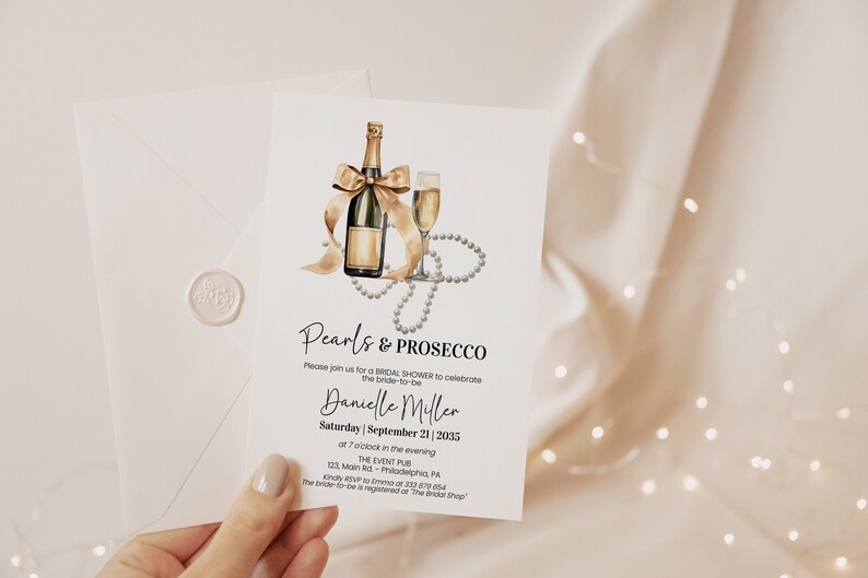 May include: A white invitation card with gold lettering for a bridal shower. The invitation features a watercolor illustration of a champagne bottle with a bow, a champagne flute, and a pearl necklace. The text on the card reads "Pearls & Prosecco" and includes the bride-to-be's name, the date, and the time of the event.