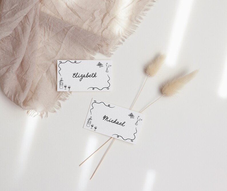 May include: Two white place cards with black calligraphy and simple illustrations. The cards read "Elizabeth" and "Michael".