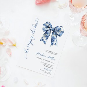 Puede incluir: Un lazo floral azul y blanco sobre un fondo blanco. El texto "she's tying the knot!" est&aacute; escrito en cursiva azul en el lado izquierdo de la imagen. El texto "Madison Miller" est&aacute; escrito en cursiva azul debajo del lazo. El texto "Saturday, April 10th at 11 am" est&aacute; escrito en azul debajo del nombre. El texto "The Garden View Hotel" est&aacute; escrito en azul debajo de la fecha. El texto "133 Riverside Street, Philadelphia, PA" est&aacute; escrito en azul debajo del nombre del hotel. El texto "Kindly RSVP" est&aacute; escrito en azul debajo de la direcci&oacute;n. El texto "Regrets only to Emma at 215-555-1212" est&aacute; escrito en azul debajo de la RSVP.