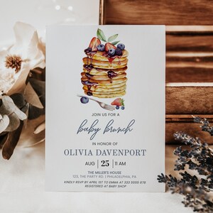 May include: A baby shower invitation with a watercolor illustration of a stack of pancakes topped with blueberries, strawberries, and syrup. The text reads "Join us for a baby brunch in honor of Olivia Davenport, Aug 25, 11 AM, The Miller's House, 123, The Party Rd. | Philadelphia, PA, Kindly RSVP by April 1st to Emma at 333 5655 678, Registered at Baby Shop."