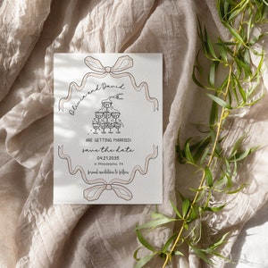 May include: Save the date card with a pink and white ribbon design. The card features a drawing of a champagne tower and the text "Olivia and David are getting married! Save the date 04.21.2035 in Philadelphia, PA. Formal invitation to follow."