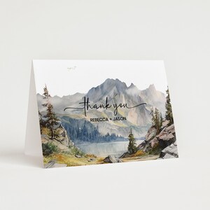 K&ouml;nnte beinhalten: Eine Aquarell-Dankeskarte mit einer Bergszene. Die Karte zeigt einen See, Berge, B&auml;ume und den Text "Danke" mit den Namen "Rebecca + Jason" darunter.