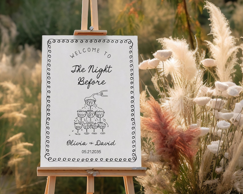 May include: White sign with black text and a drawing of champagne glasses. The text reads "Welcome to The Night Before Olivia + David 05.21.2035".