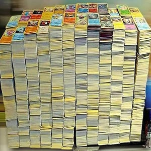 May include: A large, dense collection of rectangular trading cards stacked in multiple vertical columns. Each card features colorful graphic illustrations and text on the top surface, while the sides of the stacks show white edges.