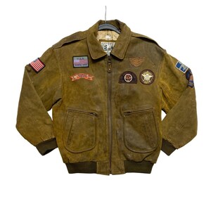 May include: A brown leather bomber jacket featuring a front zipper, ribbed cuffs and hem, and a collar. The jacket is decorated with various embroidered patches, including a U.S. flag on the sleeve, a U.S.A. patch, and several circular emblems.