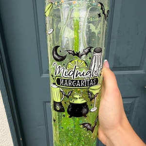 May include: A clear plastic tumbler filled with lime green liquid and glitter, featuring a green straw. The exterior displays black graphics of bats, a margarita glass, a salt shaker, a blender, and a cauldron, with the text Midnight MARGARITAS.