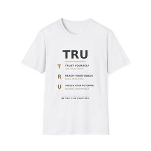 Op de afbeelding: Een wit t-shirt met korte mouwen en de tekst TRU in grote zwarte letters. Daaronder worden de letters T, R en U gedefinieerd met zinnen: TRUST YOURSELF, LIVE YOUR TRUTH, REACH YOUR GOALS, BUILD RESILIENCE, UNLOCK YOUR POTENTIAL, BECOME UNSTOPPABLE.
