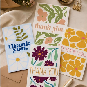 May include: Four rectangular greeting cards with floral illustrations and the text thank you. One card is light blue with white flowers, one is white with green leaves and peach flowers, one is yellow with orange flowers, and one is white with purple flowers.
