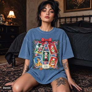 Può includere: Una t-shirt blu a maniche corte con una stampa grafica di personaggi Disney, tra cui Topolino, Minnie, Paperino, Paperina e Pluto all'interno di cornici a francobollo, decorata con un fiocco rosso, bastoncini di zucchero e il testo Merry Christmas.