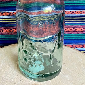 May include: A vintage green glass bottle with a wire bail closure and a white plastic lid. The bottle has a textured surface and is sitting on a wooden surface.