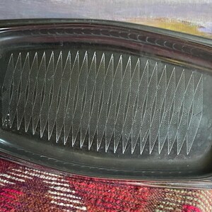 May include: A silver serving tray with a decorative pattern of lines. The tray has a slightly curved shape and a raised edge.