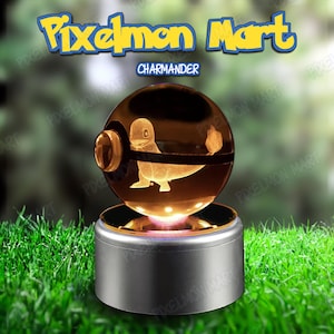Puede incluir: Una esfera de cristal con una figura de Charmander grabada con láser en su interior, que se asemeja a una Poké Ball con una banda central. La esfera descansa sobre una base cilíndrica plateada. El texto superior dice Pixelmon Mart y Charmander.