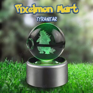 Puede incluir: Una esfera de cristal verde transparente con una figura 3D grabada con láser en su interior que representa a la criatura Tyranitar, sobre una base cilíndrica plateada. El texto Pixelmon Mart y Tyranitar aparece en azul y amarillo.