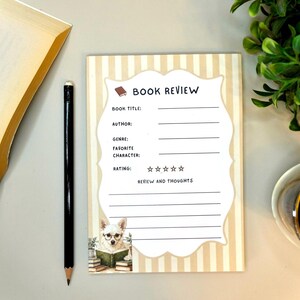 May include: A rectangular notepad with a beige and white vertical striped background featuring a central white label with the text BOOK REVIEW, fields for book title, author, genre, favourite character, rating, and review, and a small dog illustration.