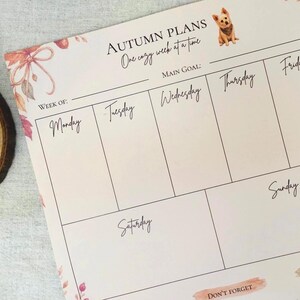 May include: A weekly planner sheet titled Autumn Plans One cozy week at a time with a small dog illustration. It features sections for Monday through Sunday, a Main Goal line, a Notes section, and a Don't Forget area, decorated with autumn leaves.