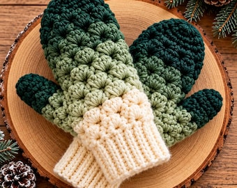 May include: A pair of crochet mittens featuring a gradient color pattern that transitions from dark forest green at the fingertips to a lighter sage green, ending in a cream-colored ribbed cuff. The texture is created with a star stitch pattern.