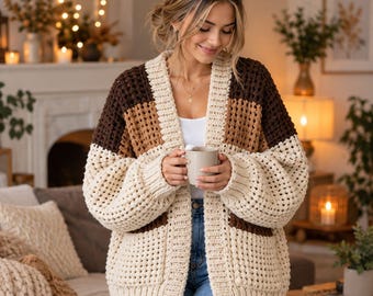May include: A chunky knit cardigan featuring a color-blocked design with horizontal stripes in cream, tan, and dark brown. The open-front garment has long sleeves, a ribbed collar, and a textured waffle-like stitch pattern throughout the body.