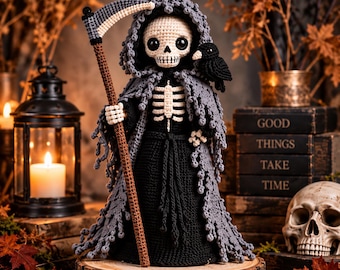 May include: A crocheted grim reaper doll featuring a white skull head with large black eyes, a black robe, and a tattered grey hooded cloak. The figure holds a brown scythe with a silver blade and has a small black bird perched on its shoulder.