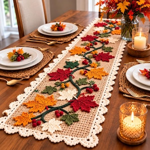 May include: A rectangular beige crochet table runner featuring a central dark green vine motif adorned with crocheted maple leaves in shades of red, orange, and cream, accented with small red and yellow berries and a scalloped cream-coloured border.