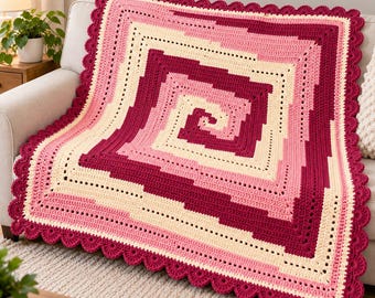 May include: A square crochet blanket featuring a geometric spiral pattern in alternating shades of cream, light pink, and deep magenta. The blanket is finished with a decorative scalloped edge border in the same deep magenta yarn color.