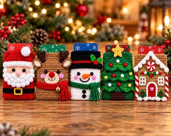 May include: Five rectangular crochet gift card holders featuring holiday designs: a Santa Claus, a reindeer with a red scarf, a snowman with a black hat, a green Christmas tree with a yellow star, and a gingerbread house with candy details.