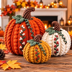 May include: Three crocheted pumpkins in orange, yellow, and white, each featuring a brown stem, green leaves, a curly green vine, and a vertical embroidered floral vine. The orange pumpkin is largest, followed by the white, then the yellow.